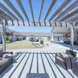 A sunny outdoor patio with a pergola casting shadows over comfortable seating and a garden view.