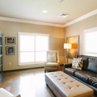 A modern living room with a leather sofa, armchair, and large windows providing natural light.