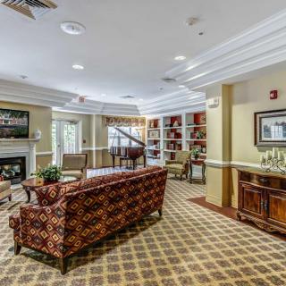 A cozy living room with a patterned couch, bookshelves, carpeted floor, and a piano.