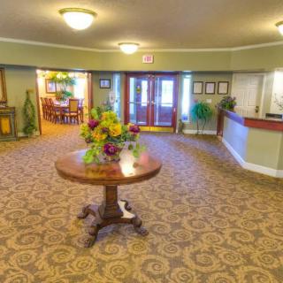 A welcoming lobby area with a round table and floral arrangement, featuring a reception desk and entrance doors.
