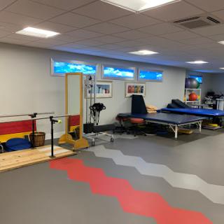 A spacious gym area designed for physical therapy and fitness training, featuring various exercise equipment and colorful flooring.