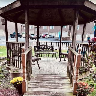 A wooden gazebo with benches, surrounded by plants and flowers in an outdoor setting.