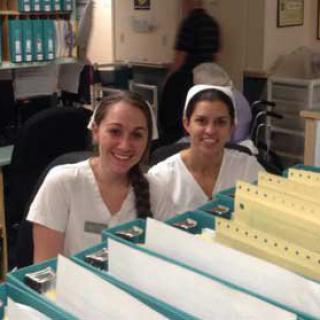 Two nurses smiling at their workstation in a hospital setting.