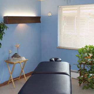 A serene massage room with blue walls and a massage table, complemented by plants for a relaxing ambiance.