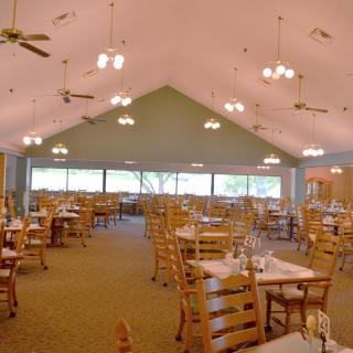 Spacious dining area with wooden tables and chairs, featuring large windows and ceiling lights.