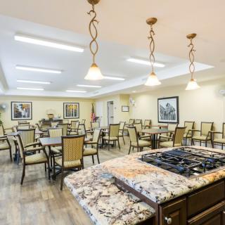 A spacious dining area with multiple tables and chairs, featuring a central kitchen island under elegant lighting fixtures.
