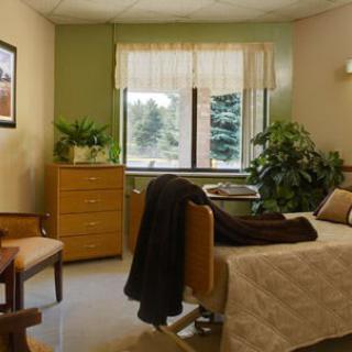 A cozy hospital room with a bed, chair, and plants by the window.