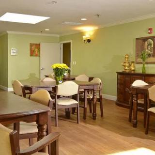 A cozy dining area with wooden tables and chairs, decorated with a flower vase on one of the tables, set against green walls.