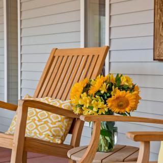 A cozy porch setting with a wooden chair, vibrant sunflowers, and a decorative cushion.