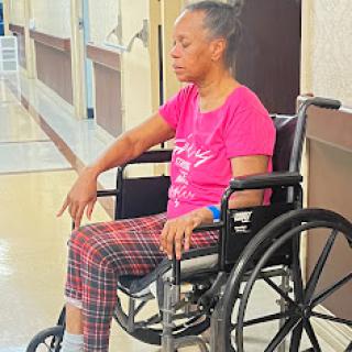 An elderly person in a wheelchair, sitting quietly in a hospital corridor.