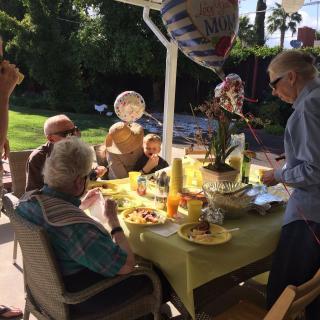 A family gathering outside for a meal, with decorations and balloons.