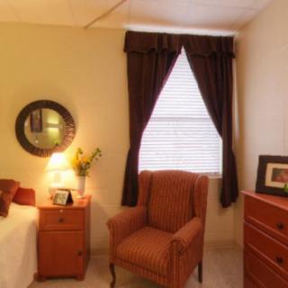 Cozy bedroom corner with an armchair, lamp, and window draped with curtains.