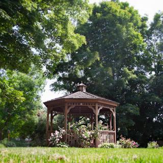 A charming wooden gazebo surrounded by lush greenery and blooming flowers.