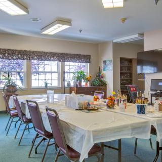 A well-lit dining or meeting room with tables and chairs arranged, featuring large windows and various decorations.