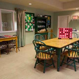 A cozy kitchen dining area with a wooden table and chairs, featuring a bulletin board and shelves in the background.