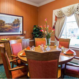 A cozy dining room with a round table set for four, decorated with a vase of flowers and surrounded by red cushioned chairs.