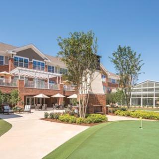 A sunny outdoor space featuring a well-designed residential building with landscaping and patio seating.