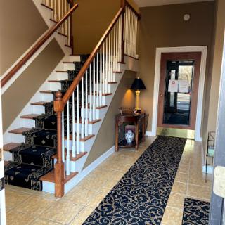 A well-lit hallway featuring a staircase, elegant decor, and a patterned rug leading to the entrance.