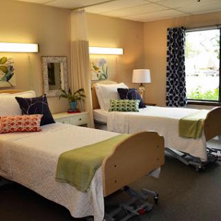 A comfortable and well-lit hospital room featuring two patient beds with decorative pillows.