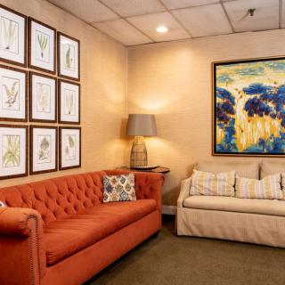 A cozy living room featuring a red sofa, a beige couch, and various artworks on the walls.