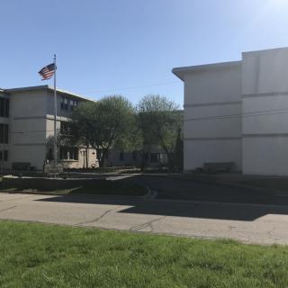 A view of a school building with an American flag and surrounding trees on a sunny day.