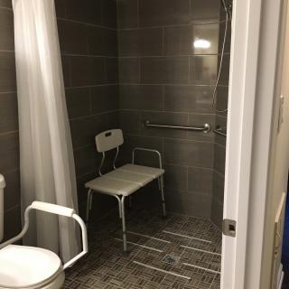 An accessible bathroom featuring a shower area with a chair and grab bar.