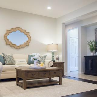 A modern living room with a cozy sofa, wooden coffee table, decorative mirror, and lamp.