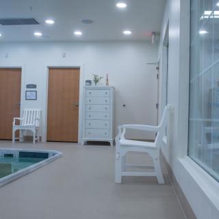 A clean and modern indoor pool area with chairs and locker room doors.