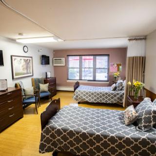 A cozy hospital room featuring two beds, a seating area, and natural light coming through the window.