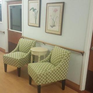 A seating area in a hallway with two patterned chairs, a small table, and framed floral artwork on the wall.