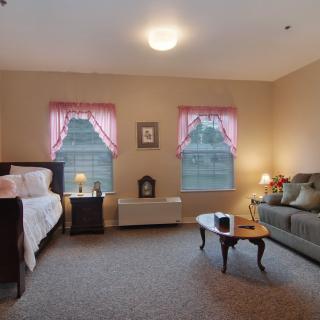 A cozy living space with a daybed, sofa, and coffee table, featuring two windows with pink curtains.