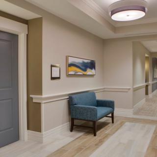 A well-lit hallway with an armchair and a painting on the wall.