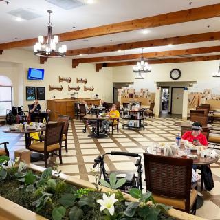 A spacious dining area with wooden beams, chandeliers, and several people seated at tables.