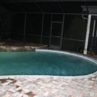A nighttime view of an enclosed swimming pool area with a paved patio.