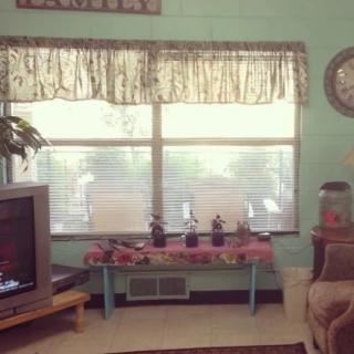 A cozy living room with a television, sofa, and large window decorated with curtains.