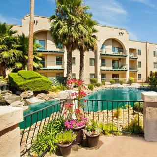 A sunny day at a residential apartment complex with a pool and lush landscaping.
