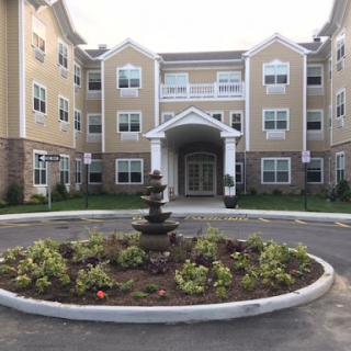 A modern residential building featuring a welcoming entrance and decorative landscaping with a fountain.