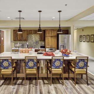 A modern kitchen with a large island and colorful seating, featuring pendant lighting and wooden cabinets.