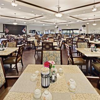 A spacious dining room with multiple tables and chairs, set for meals in a formal restaurant environment.