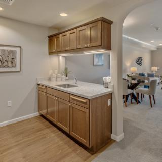 A modern kitchenette with wooden cabinets and a sink, leading to an open dining area.