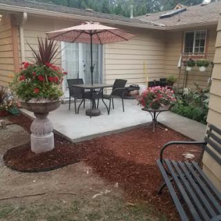 A cozy patio area featuring a table and chairs under an umbrella, surrounded by vibrant flowers and well-maintained landscaping.