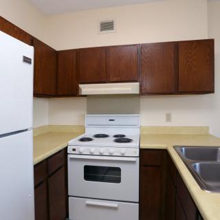 A compact kitchen with wooden cabinets, a stove, refrigerator, and dual sink.