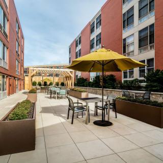 A modern outdoor patio area with tables, chairs, and umbrellas set between two buildings.