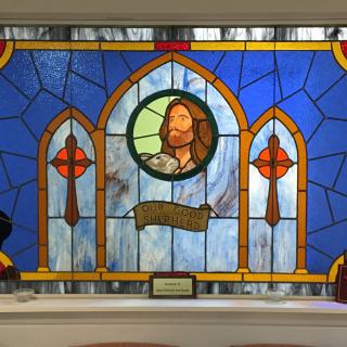 A stained glass window featuring a depiction of Jesus in a church setting.