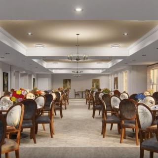 An elegant dining room with neatly arranged tables and chairs, illuminated by chandeliers.