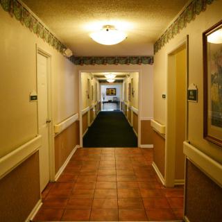 A well-lit hotel hallway with doors and framed artwork along the walls.