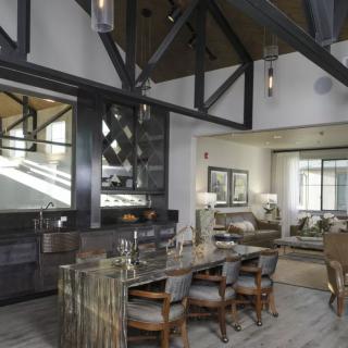 A modern open-plan living area with a dining table, kitchen, and cozy seating arrangement, featuring high wooden beam ceilings.