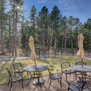 A scenic patio with wrought iron furniture and umbrellas set amidst a backdrop of lush trees and a clear blue sky.