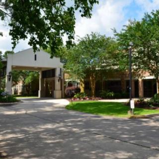 A building with a covered entrance surrounded by trees and a driveway.