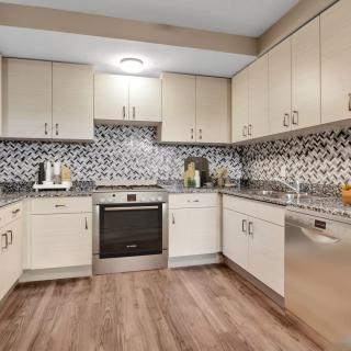 A modern kitchen featuring white cabinets, a patterned backsplash, and hardwood flooring.